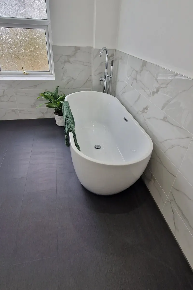 After: freestanding bath under the window with marble-effect wall tiles and dark floor