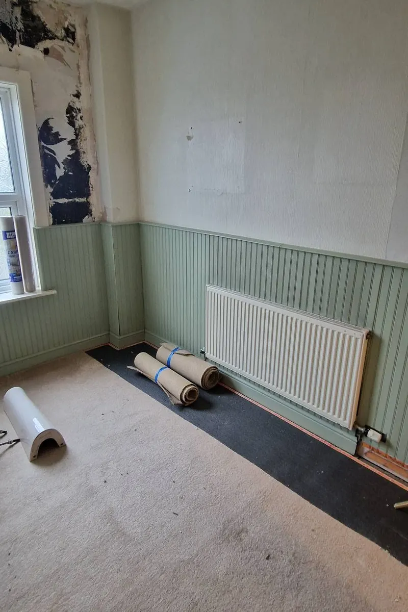 Before: stripped room with old green panelling, a radiator and rolled-up flooring