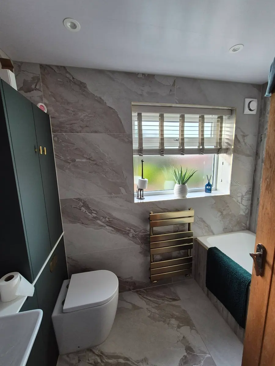 Bathroom with marble-effect tiles, green bath panel, tall green unit and gold towel rail