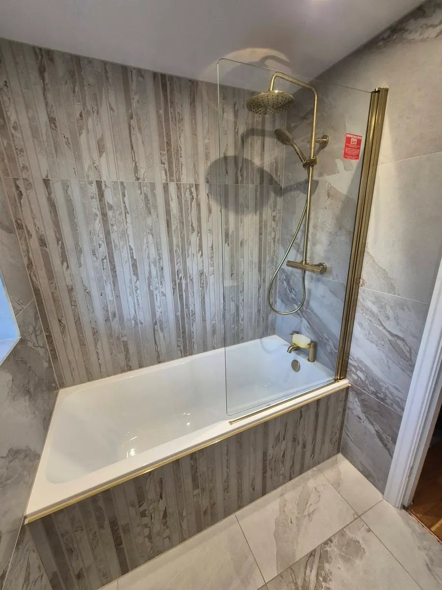 Shower over a bath with a brushed brass shower set and wood-effect wall panels