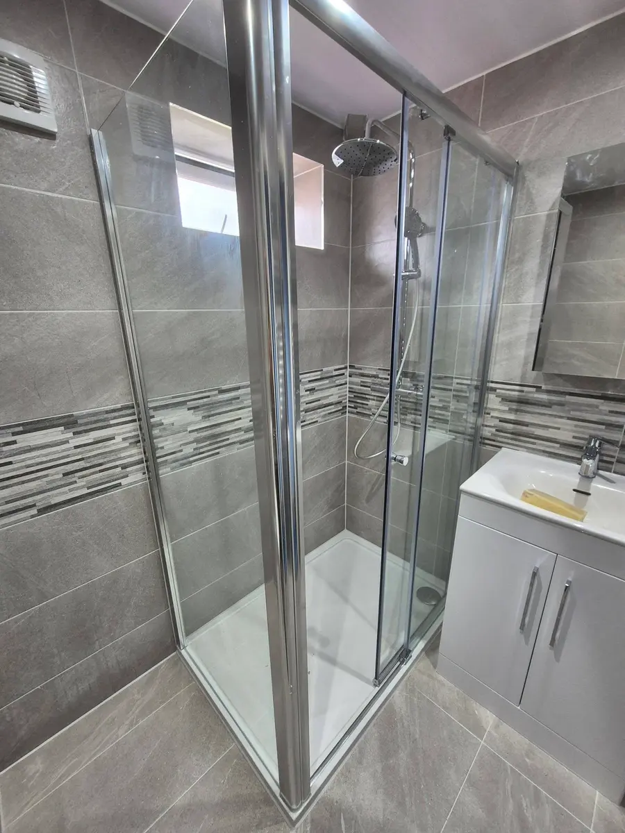 Sliding shower enclosure with grey tiles and a mosaic border