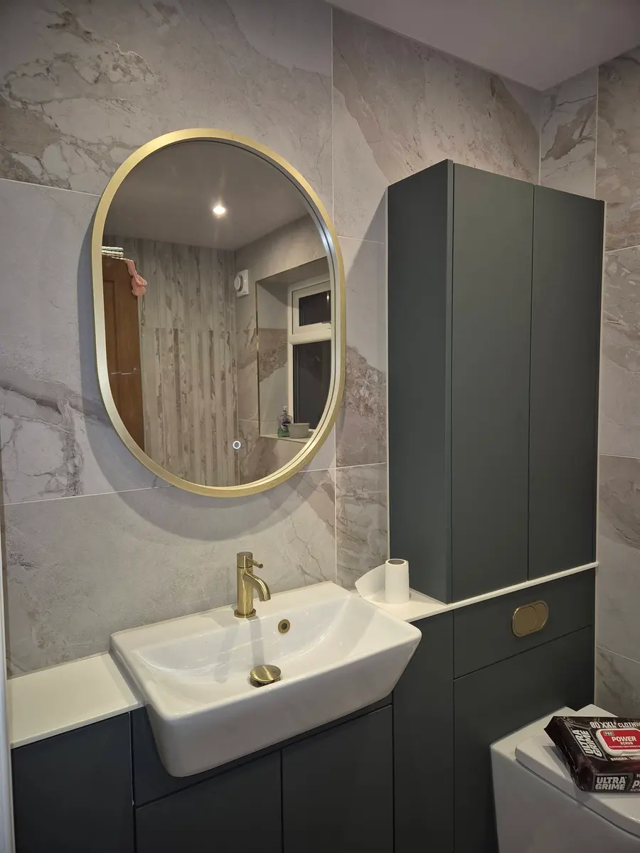 Basin on a sage green vanity unit with a brushed brass tap and round brass mirror